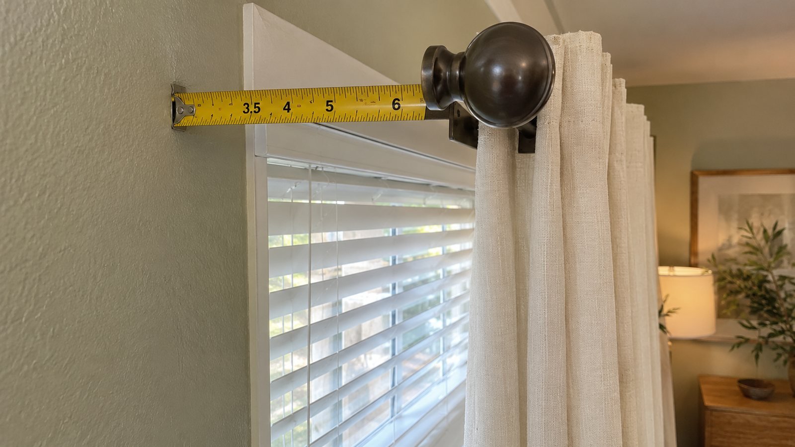 tape measure showing 3.5–6 in (9–15 cm) return/projection from wall past blind headrail on cream sage rental window